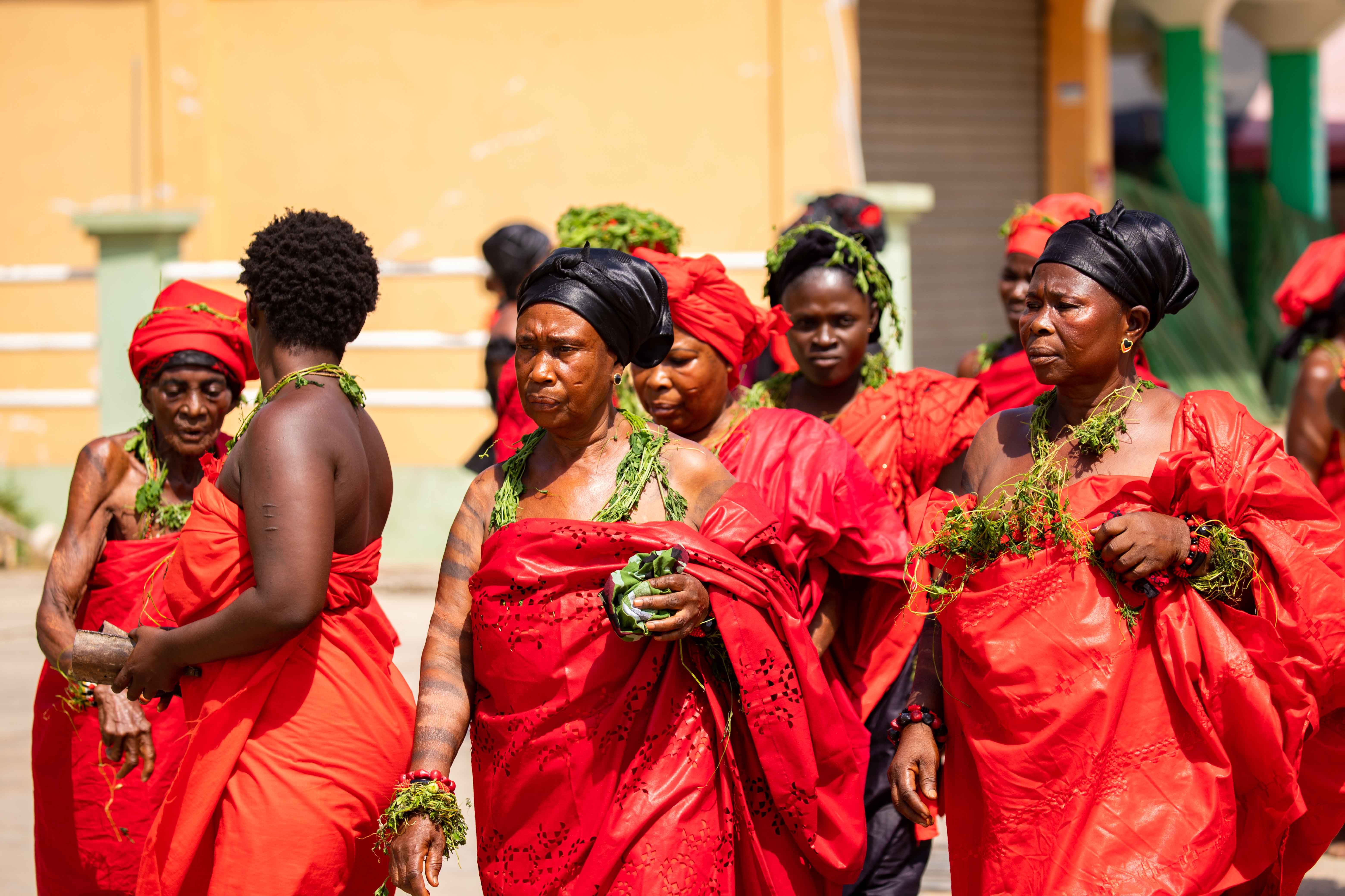 A group of women in vibrant red traditional attire participate in a cultural ceremony outdoors.