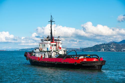 Free A vibrant red tugboat navigates the calm blue sea under a clear sky with clouds. Stock Photo