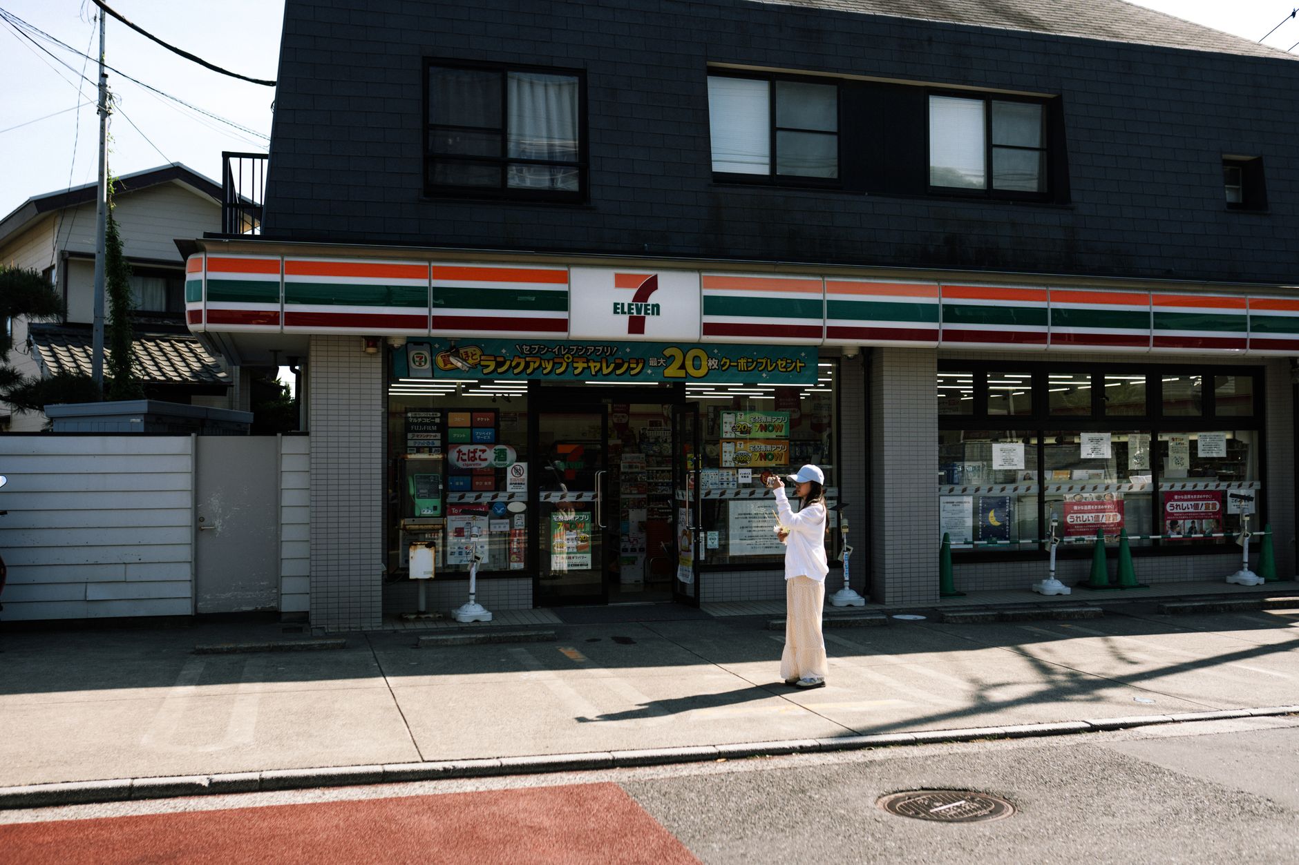 A person taking a photo outside a 7-Eleven store on a sunny day with clear skies.