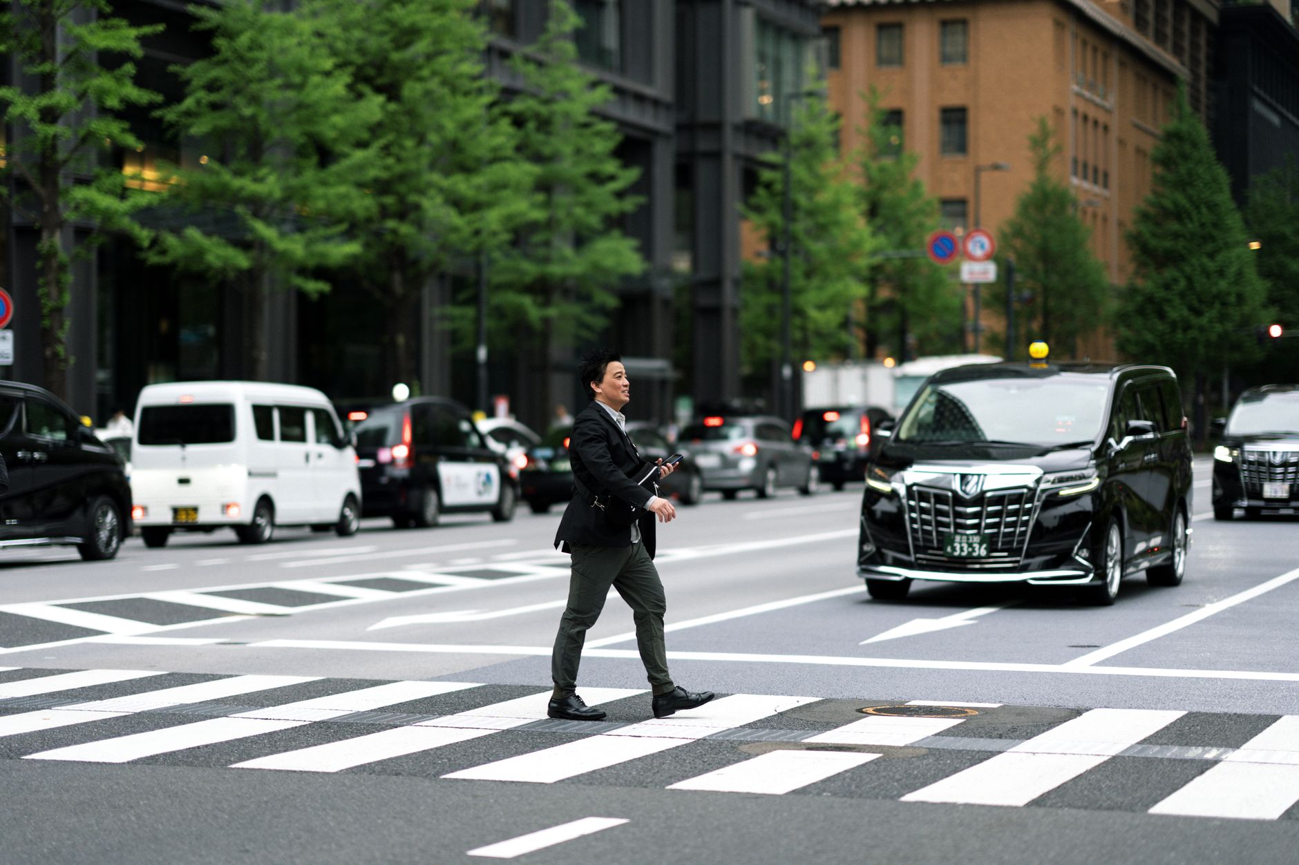A businessman walking across a busy city street in Japan with vehicles in the background.