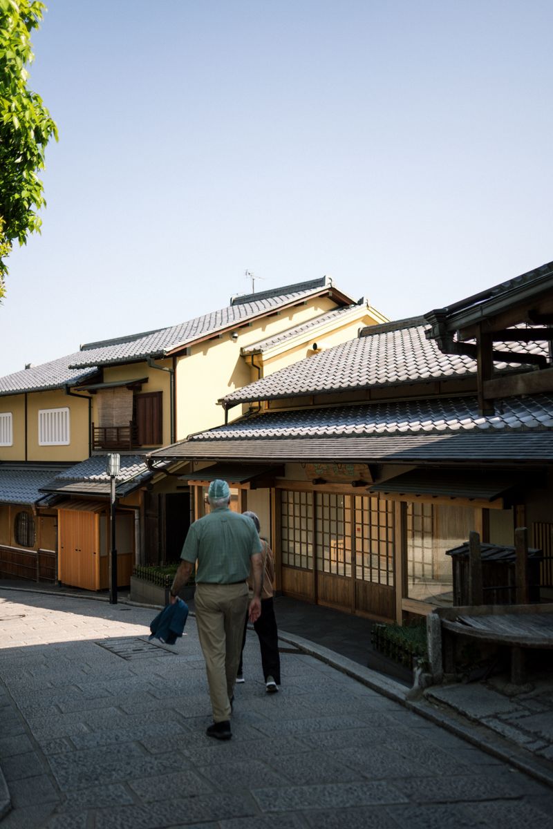 A peaceful walk along a traditional street in Kyoto with historic wooden houses under a clear blue sky.