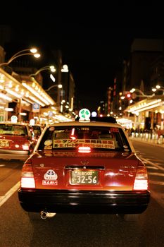 A red taxi on a bustling night street in Japan, showcasing lively urban atmosphere.