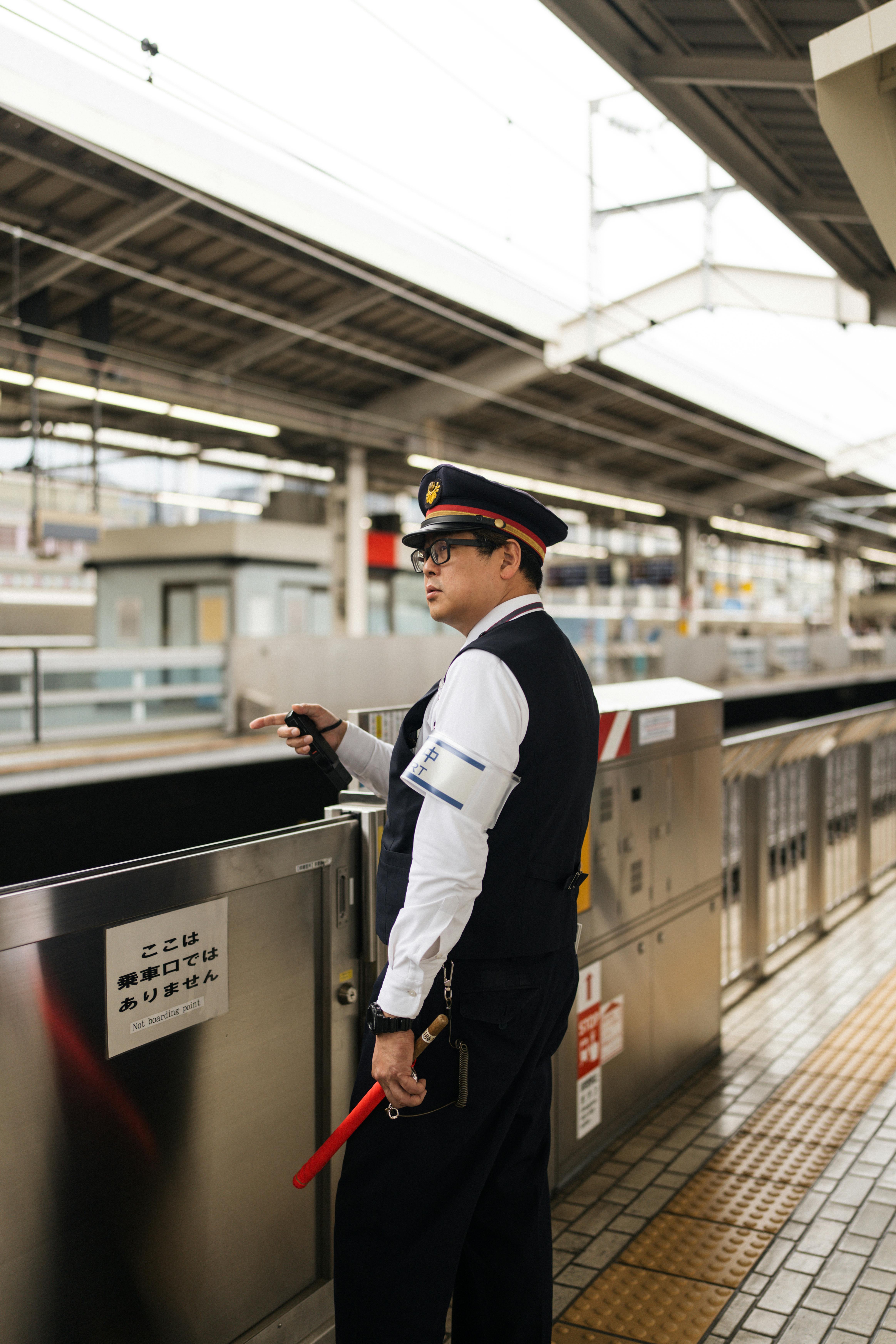 A security officer stands watch at a Japanese train station platform in uniform.