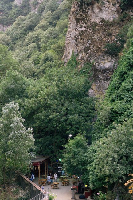 Charming outdoor cafe nestled in a lush green valley with natural rock formations.