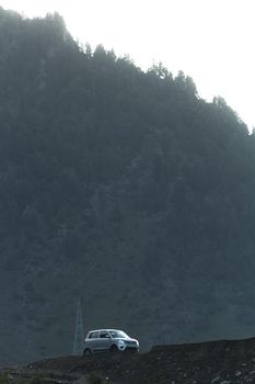SUV navigating a rural mountain road under a misty hillside setting.