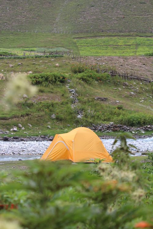 Free Vibrant yellow tent pitched beside a serene river in a lush landscape. Stock Photo
