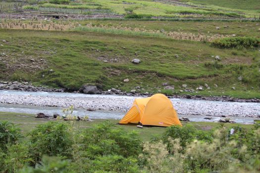A vibrant yellow tent set in a lush riverside landscape, ideal for camping enthusiasts.