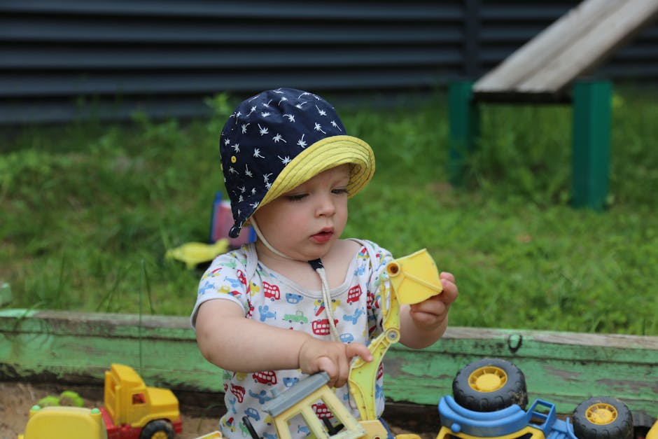 Uma criança pequena aproveita o tempo brincando ao ar livre com carrinhos de construção de brinquedo em uma caixa de areia, explorando e se divertindo.