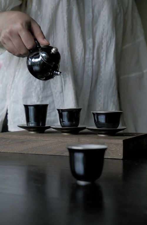 Free Elegant tea pouring scene capturing traditional Vietnamese practice with black teapot and cups. Stock Photo