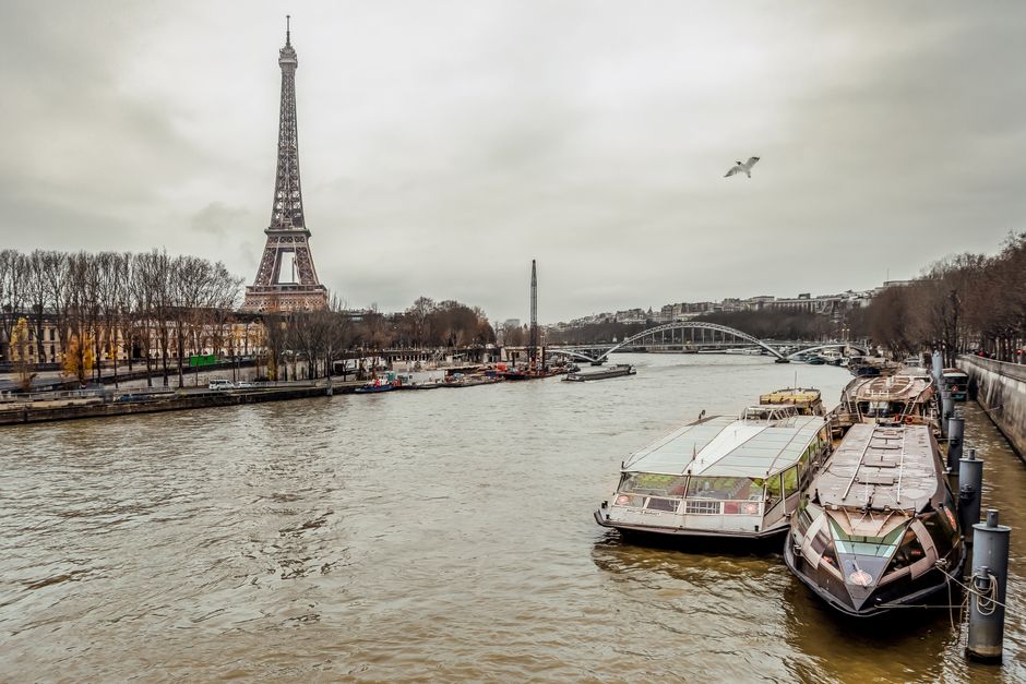 Scenic view of the Eiffel Tower and Seine River with moored boats on a cloudy day.