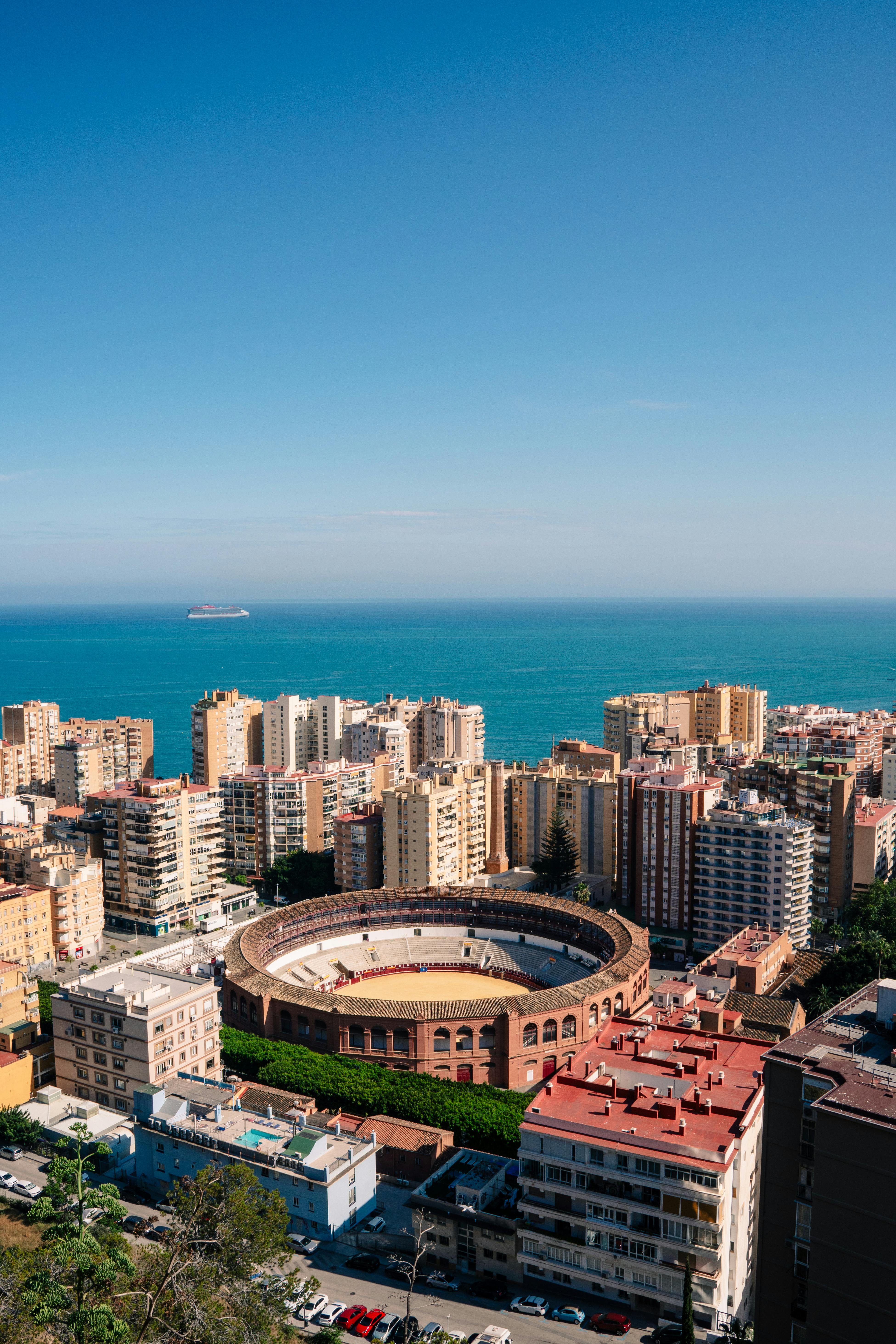 A stunning aerial view of Málaga's iconic bullring and the coastal cityscape under a clear blue sky.