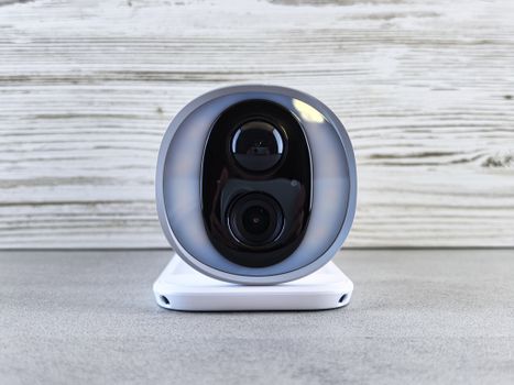 Close-up of a smart security camera with a modern design on a gray surface indoors.