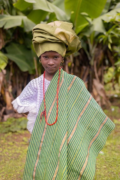 Free Young girl in colorful traditional African attire standing amidst lush greenery outdoors. Stock Photo