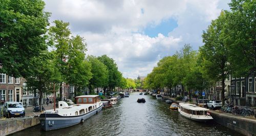 Free Picturesque view of Amsterdam canal with boats and lush trees under a cloudy sky. Stock Photo