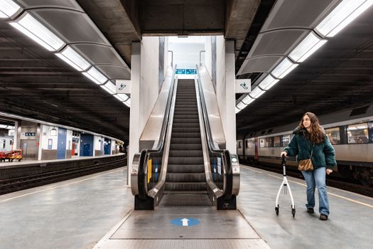 A woman with a rollator at an empty modern train station platform near an escalator.