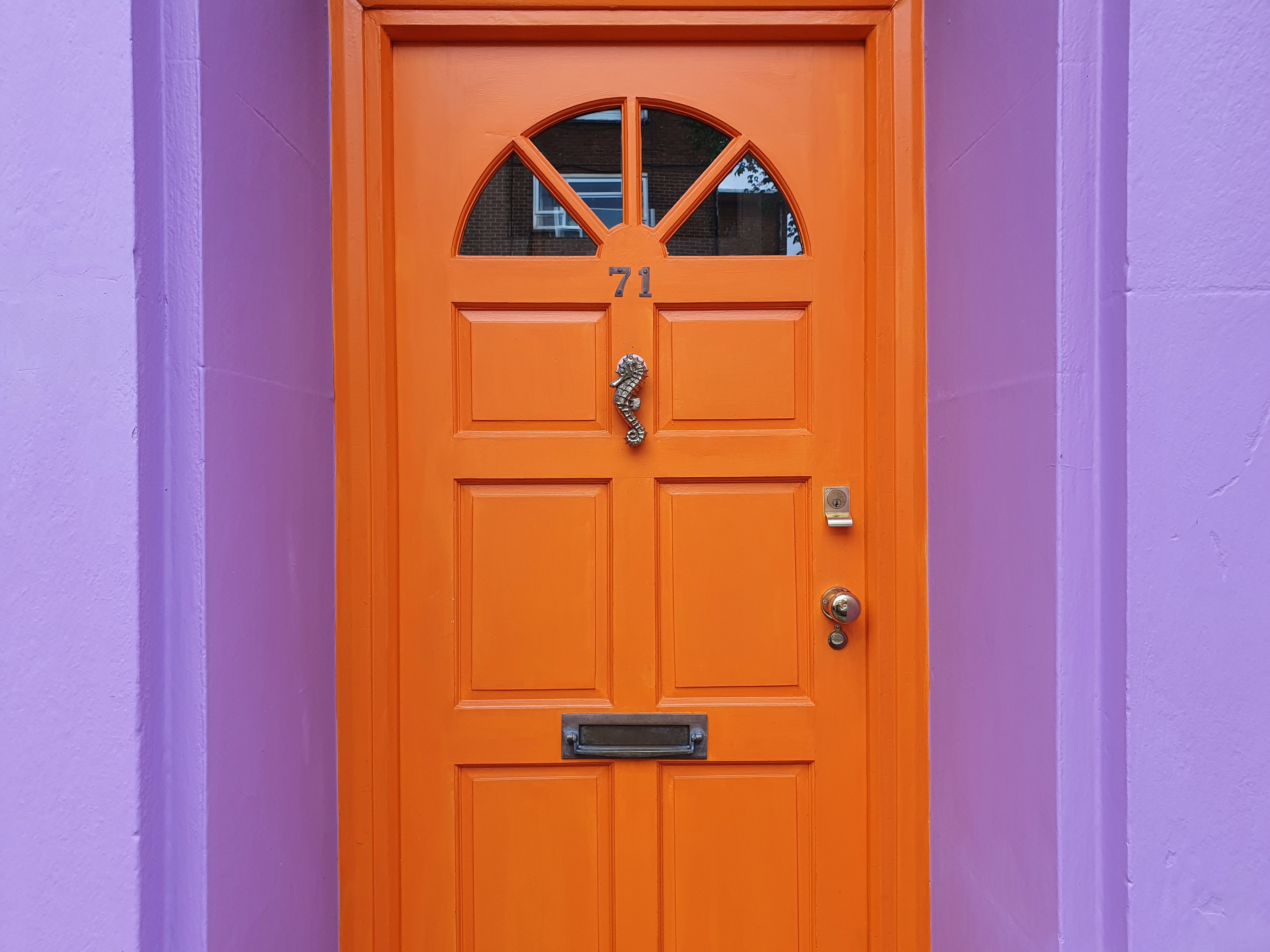 A striking orange door with a seahorse knocker against a purple wall, numbered 71.