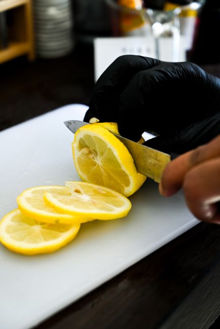 Person slicing a lemon on a cutting board with knife and gloves, indoors.
