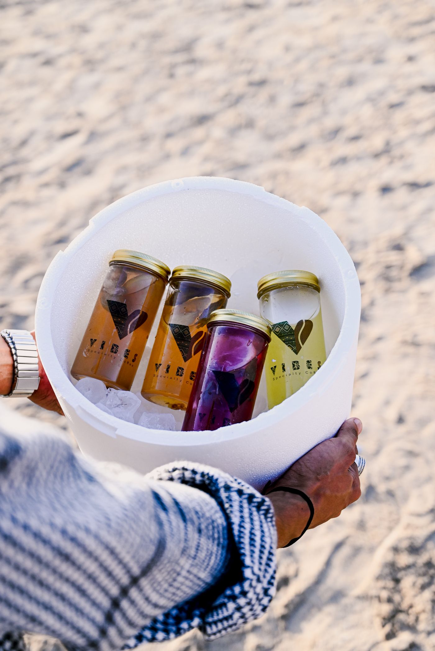 Portable cooler with refreshing drinks arranged on beach sand