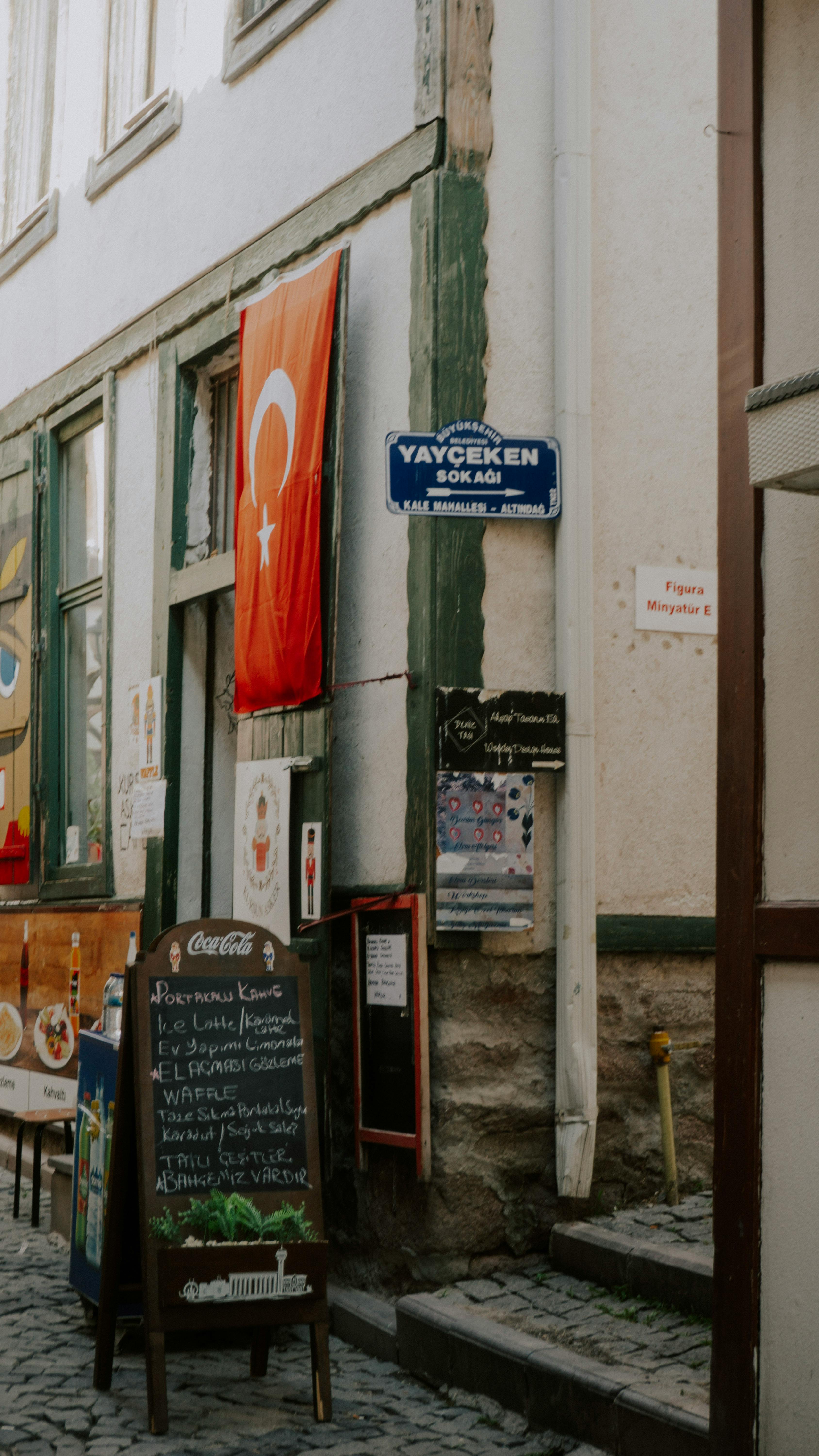 Narrow Turkish street with a cafe, flag, and signs, capturing local architecture and culture.