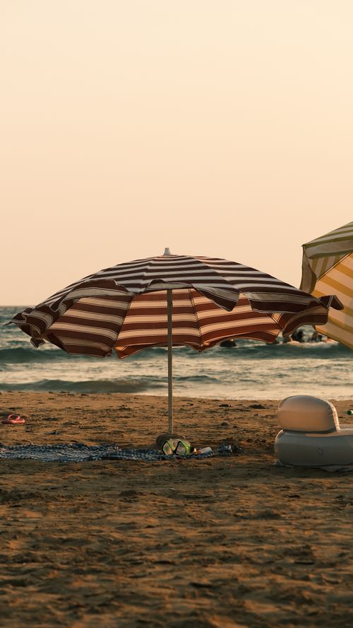 Free A striped beach umbrella on a sandy shore during sunset, evoking a serene summer vibe. Stock Photo