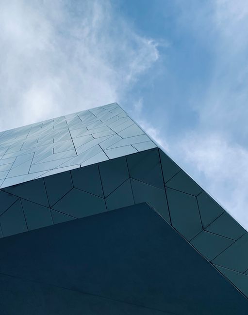 Low-angle view of a modern building facade against a blue sky, showcasing geometric design.