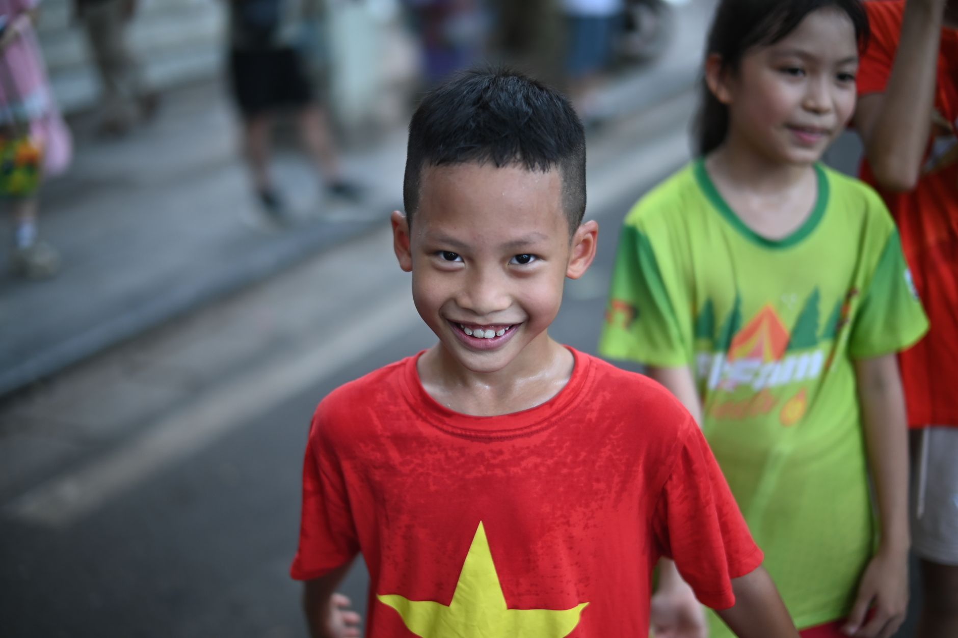 Cheerful child in a red shirt with a yellow star enjoying time outdoors, soaking wet from fun activities.