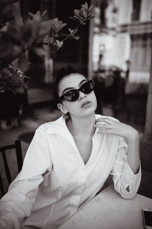 Free Stylish woman in sunglasses poses elegantly in a modern cafe setting, capturing timeless fashion. Stock Photo