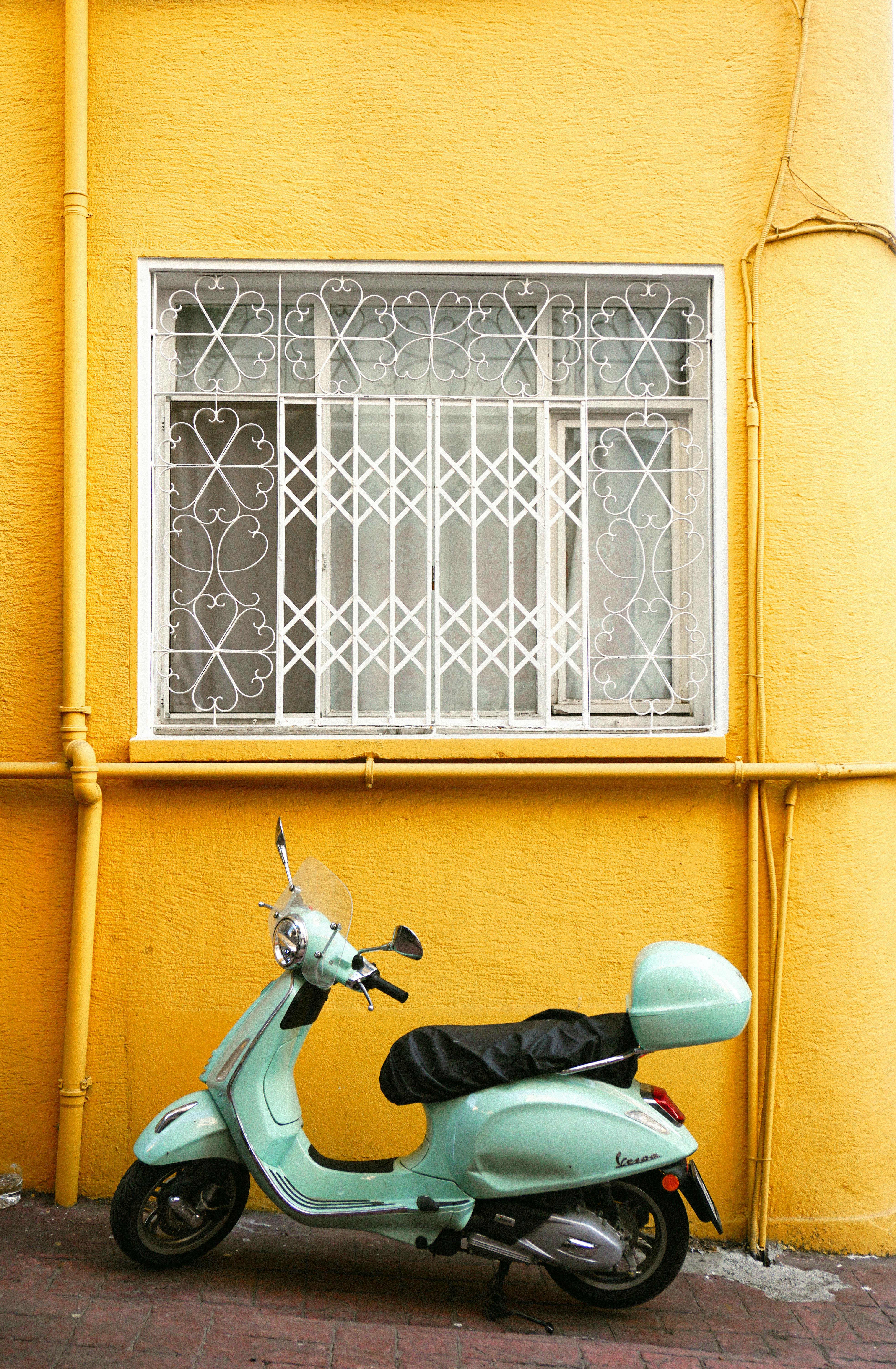 Stylish mint green scooter parked by a vibrant yellow wall with decorative window.