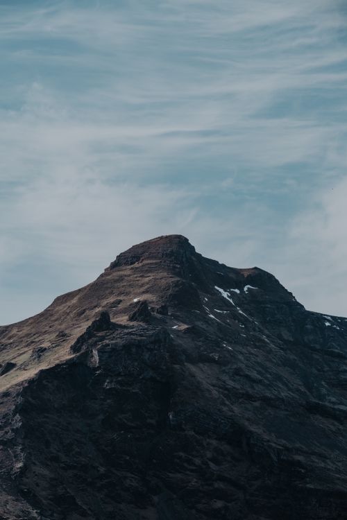 Free Majestic mountain peak reaching into cloudy sky in a dramatic landscape. Ideal for nature and travel themes. Stock Photo