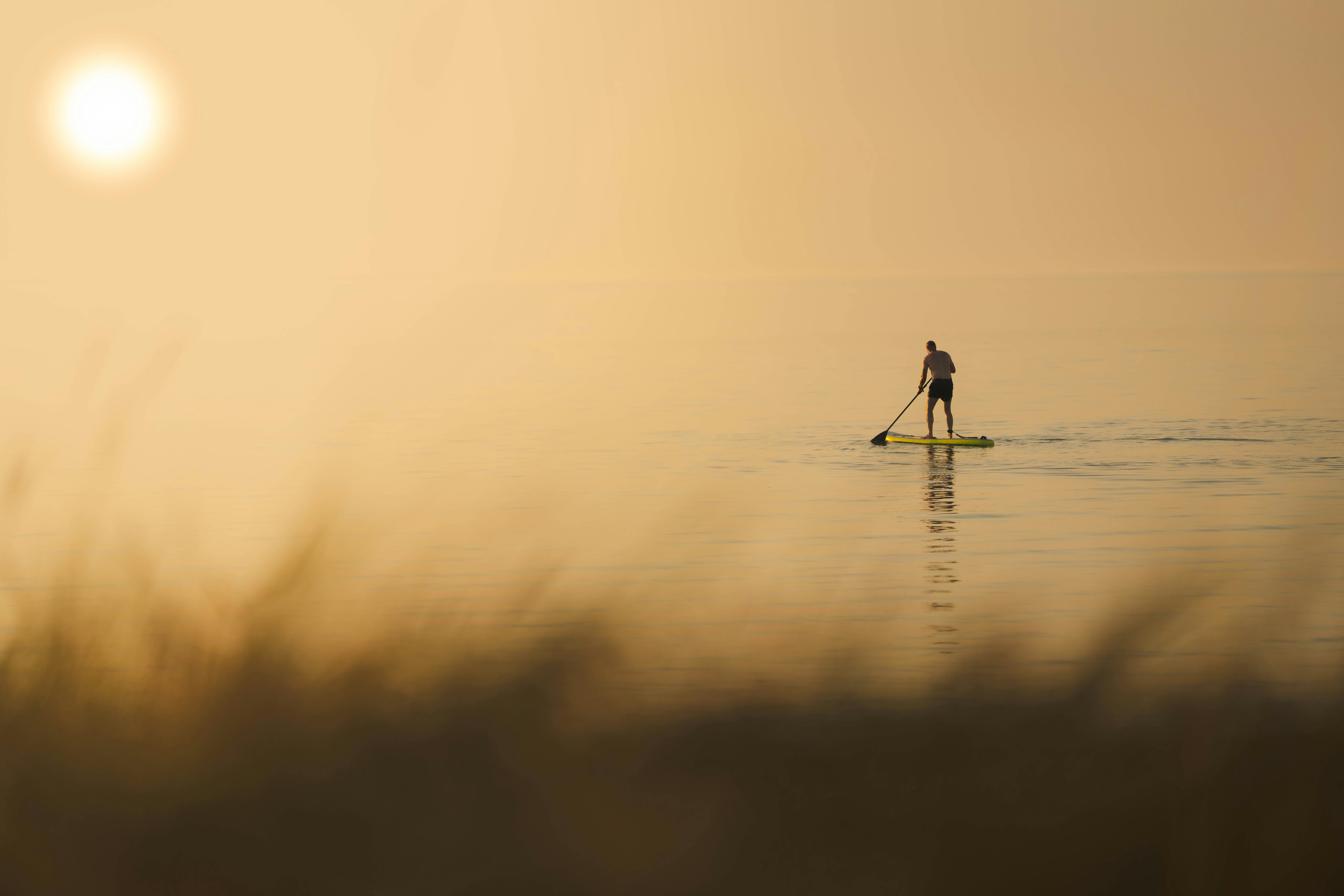 A lone person paddleboarding on a tranquil sea during sunset, creating a peaceful and calm scene.