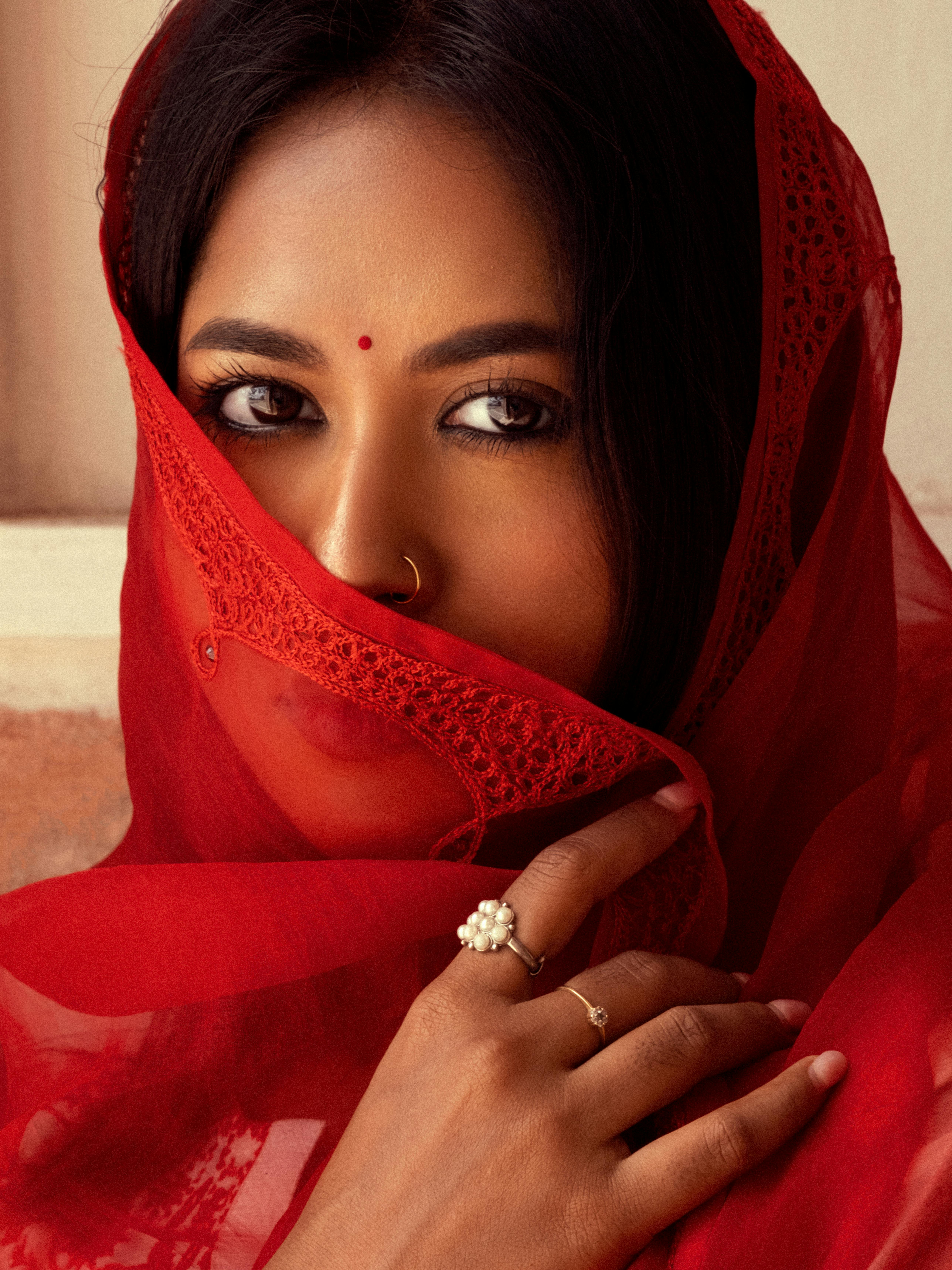 Portrait of a South Asian woman wearing a red traditional veil with intricate patterns.