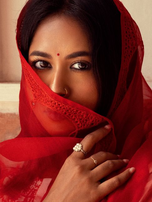 Portrait of a South Asian woman wearing a red traditional veil with intricate patterns.