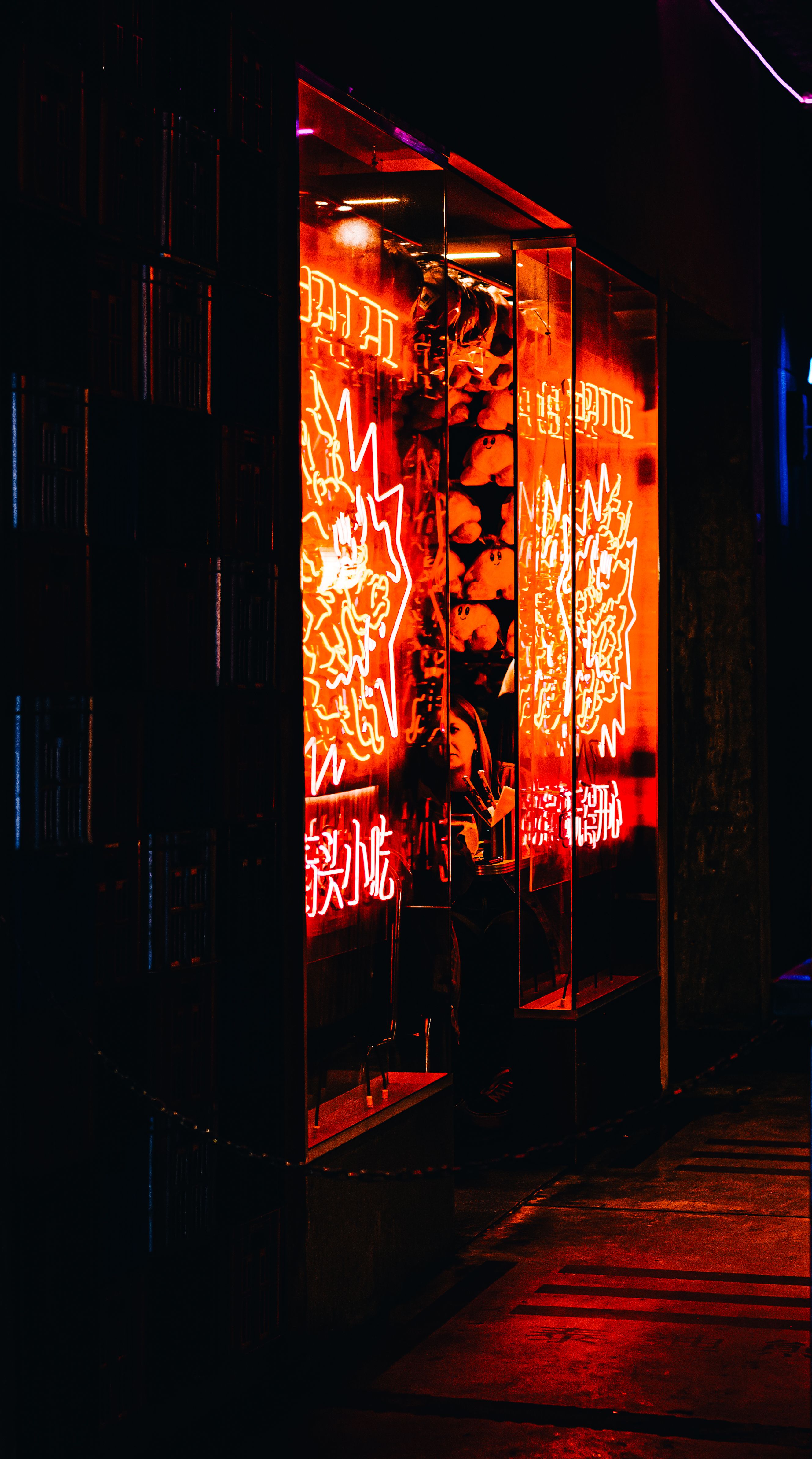 A striking display of red neon lights in an urban setting at night, reflecting on a shop window.