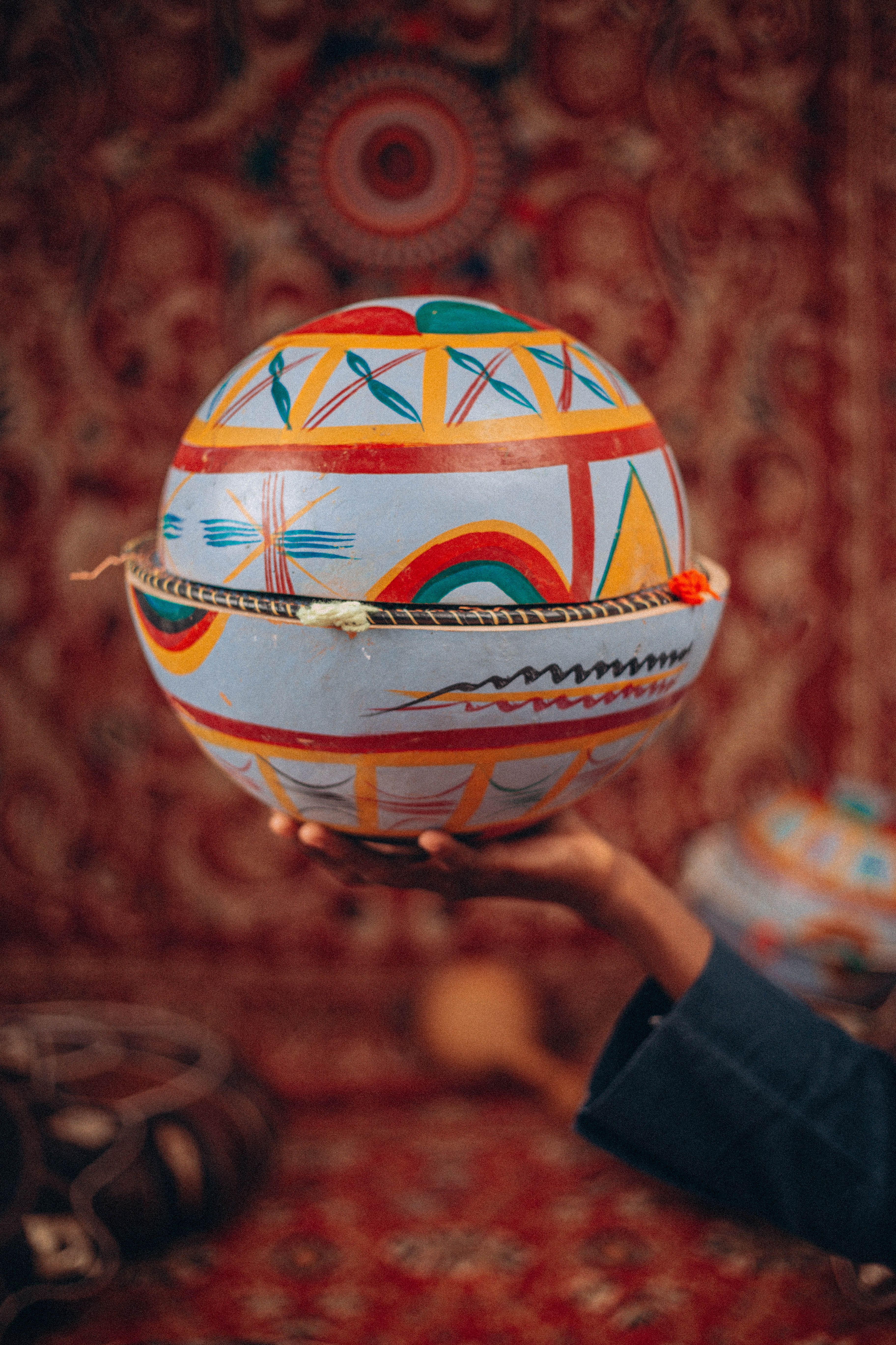Vibrant handcrafted sphere with intricate tribal patterns held by an adult hand.