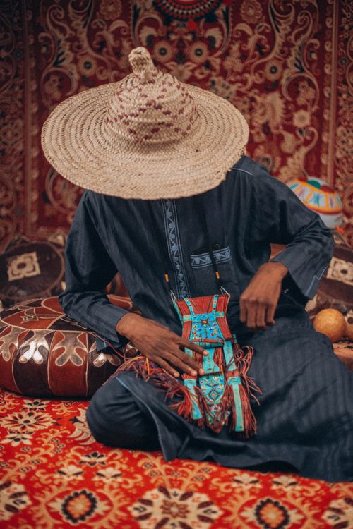 Free Man in traditional African attire with straw hat sitting on colorful textile background. Stock Photo
