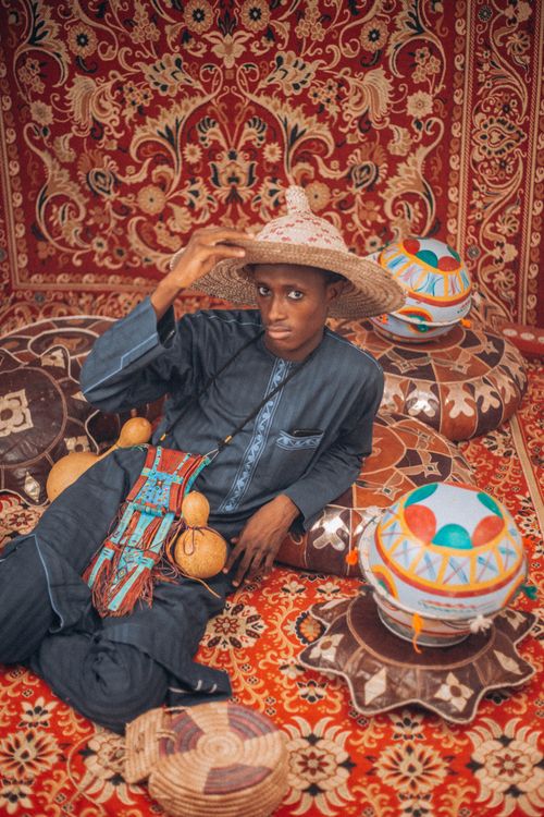 Free A man in traditional attire sits amidst colorful, patterned cushions and carpet. Stock Photo