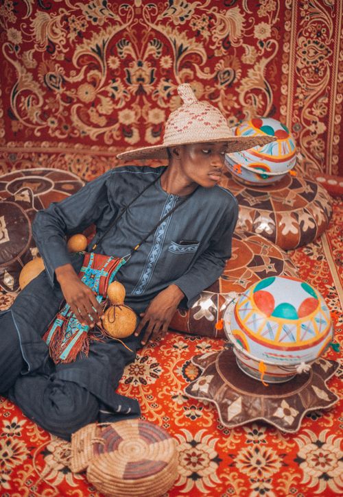 Free Young man in traditional African attire surrounded by colorful cultural patterns and textures. Stock Photo