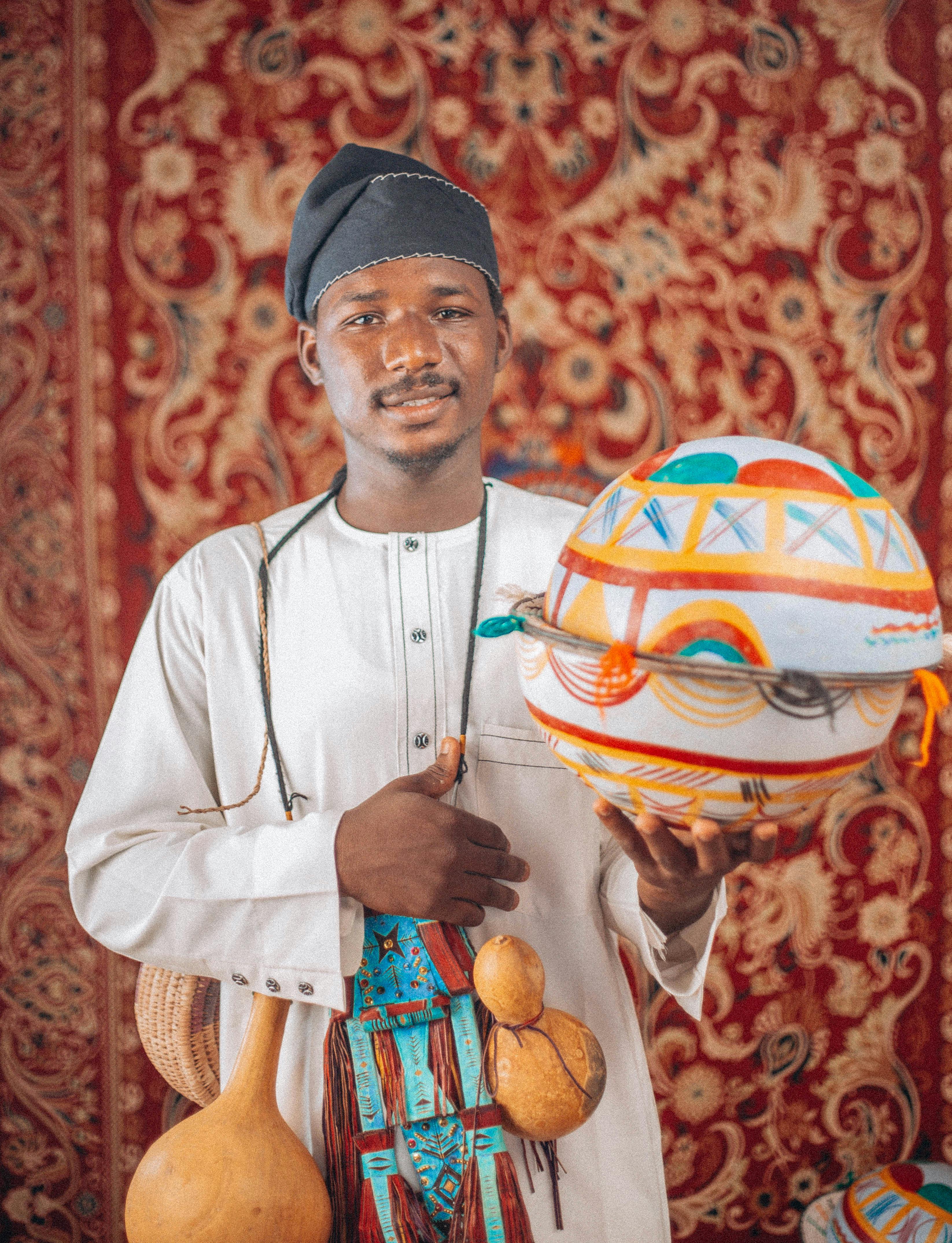 African man in traditional attire holding a decorated gourd, showcasing cultural heritage.