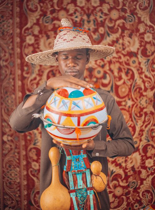 Free Man wearing a traditional hat holding an African decorated calabash in front of ornate backdrop. Stock Photo