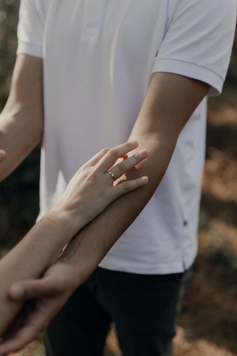 A close-up of a couple touching hands outdoors, symbolizing connection and affection.