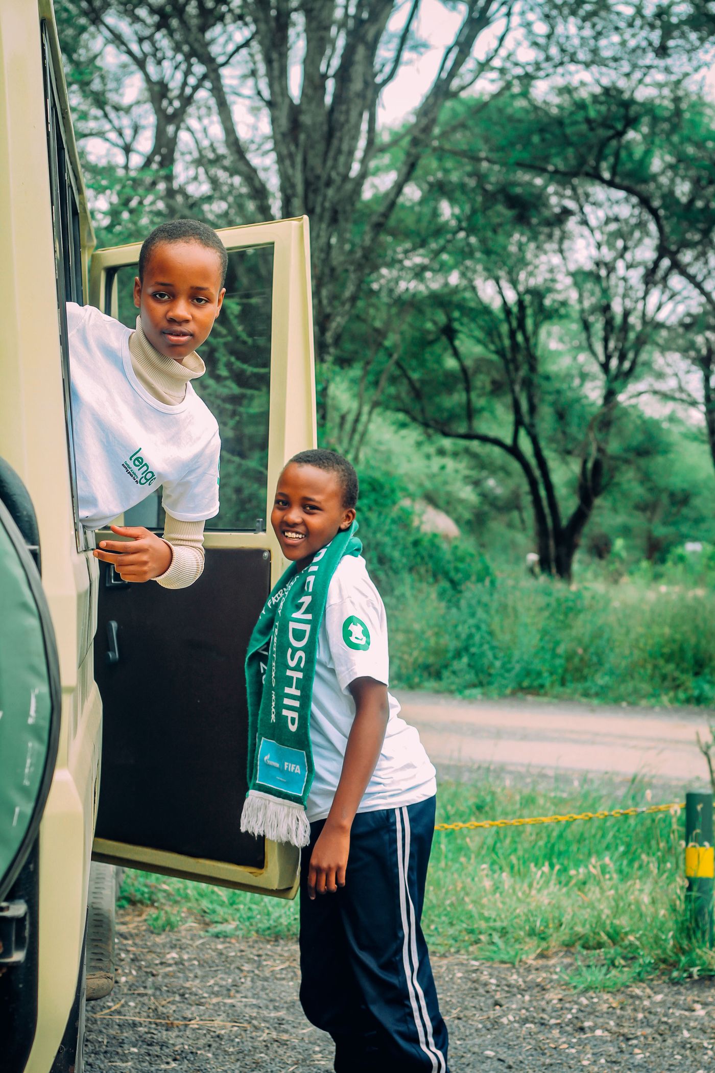 Two children in safari clothing smiling from an open game-drive vehicle in Africa