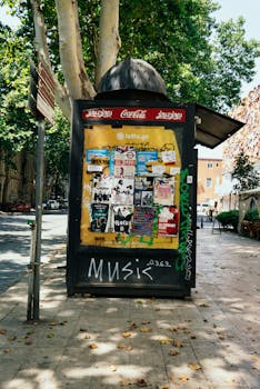 Street billboard displaying posters and graffiti, set in a sunny urban area in Tbilisi, Georgia.