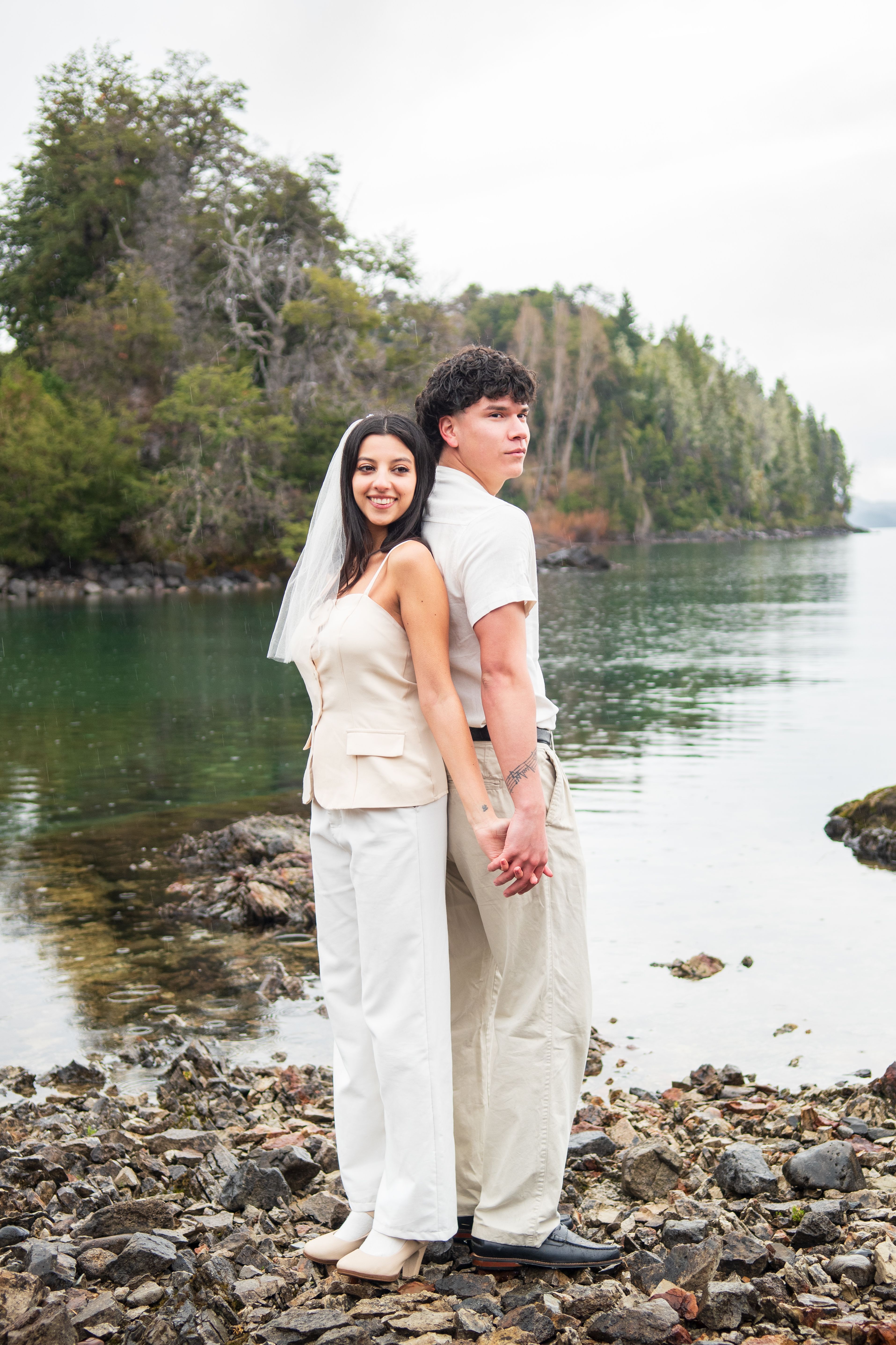 A happy couple holding hands by the serene Lake Nahuel Huapi in Bariloche, Argentina.