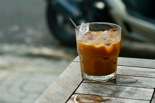 Free Close-up of a refreshing iced coffee in a glass with ice cubes on an outdoor wooden table. Stock Photo