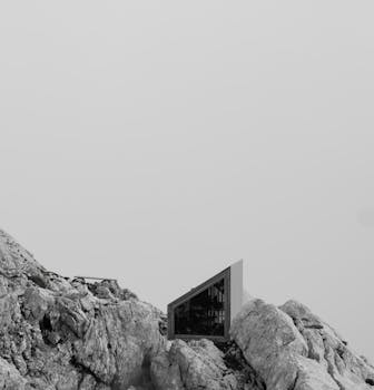 Minimalist mountain shelter placed among rocky terrain under overcast sky.