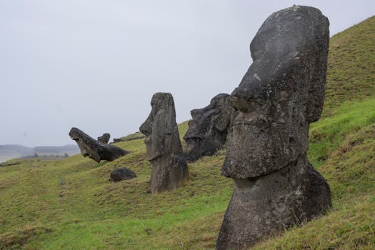 Moai statues standing on grassy hills in Easter Island, Chile under a cloudy sky.