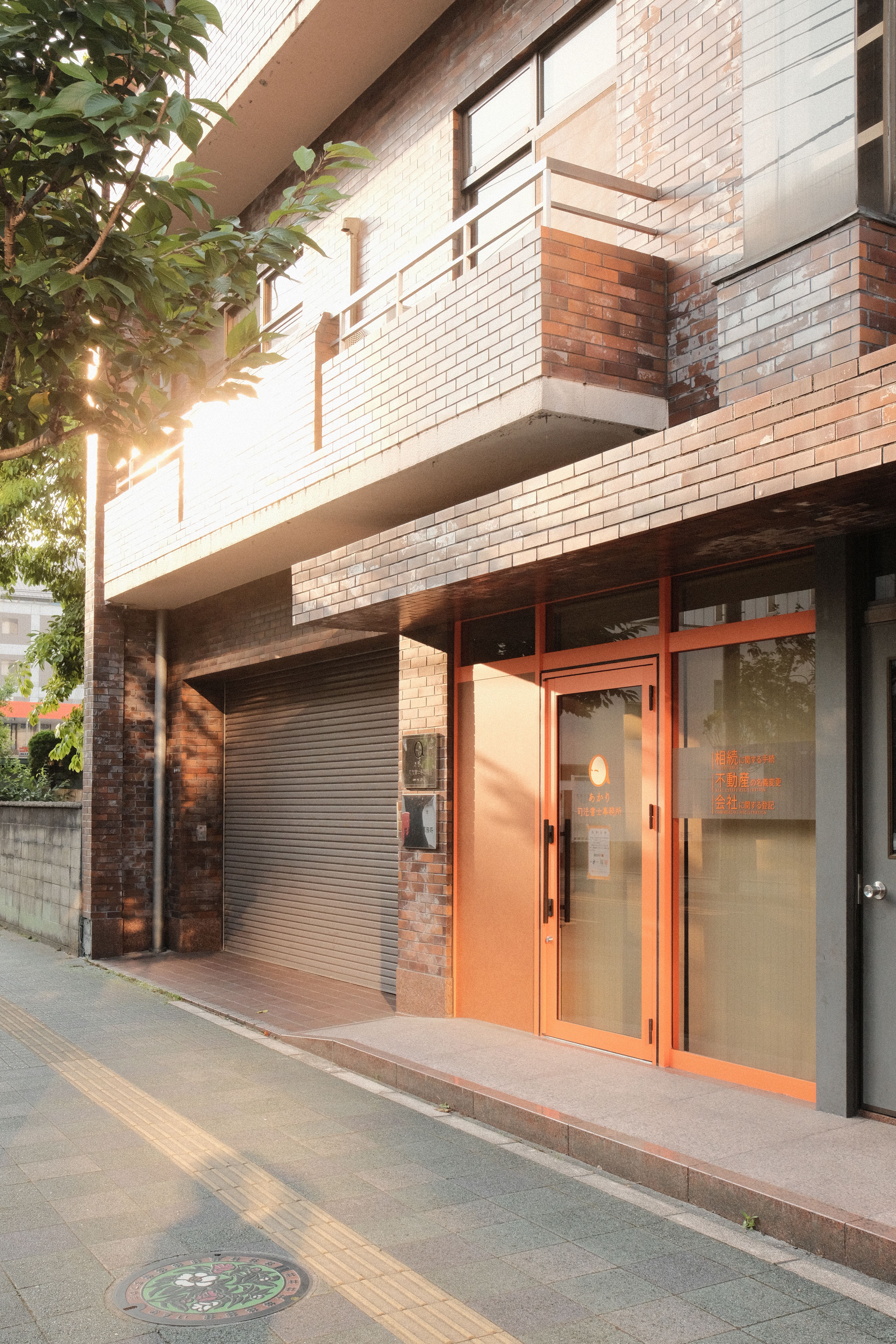 Facade of sunlit brick building with glass entrance on a quiet city street.