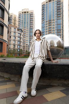 A stylish young adult poses outside modern city buildings, exuding confidence.