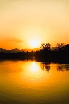 A breathtaking view of a sunset casting golden hues over a calm lake and distant mountains.
