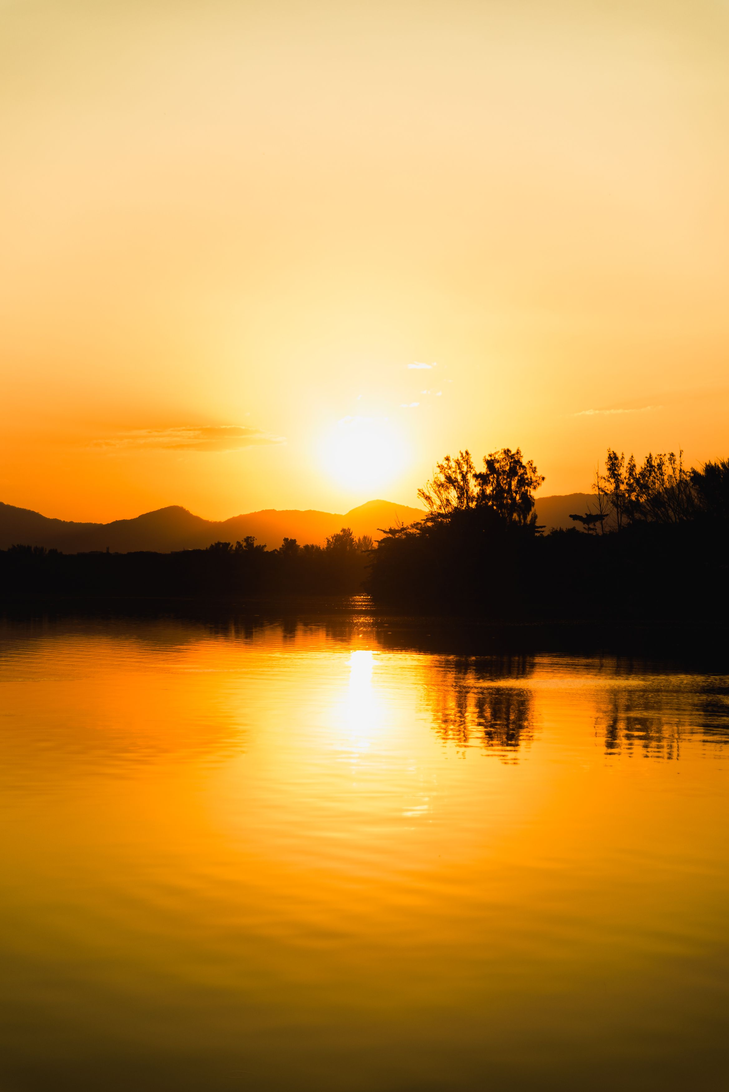 De franc Una vista impressionant d'una posta de sol que projecta tons daurats sobre un llac tranquil i muntanyes distants. Foto d'estoc